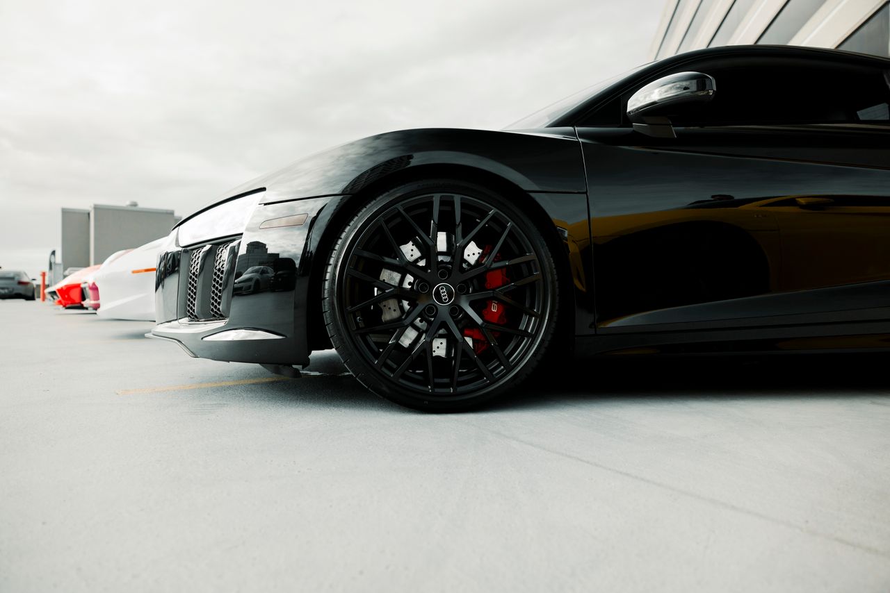 team-02 Close-up of a black luxury sports cars wheel detail in an outdoor setting.