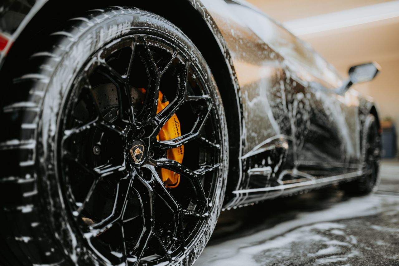 services-02 Detailed close-up of a luxury car wheel covered in soap suds during a professional car wash.